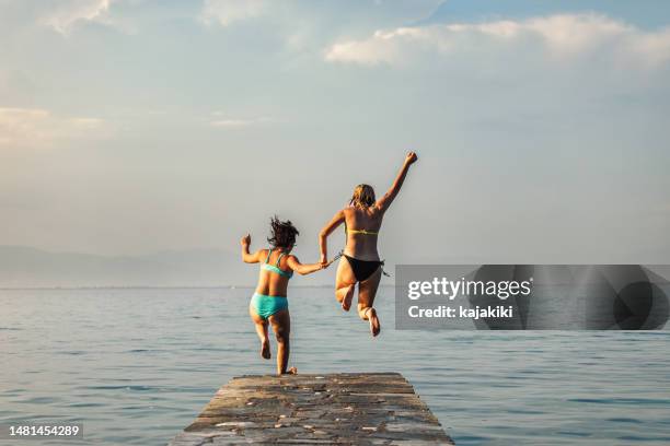 dos adolescentes saltando desde el muelle al mar azul - girl diving fotografías e imágenes de stock