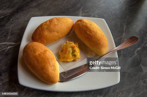 three pandebono (colombian cheese bread) rolls, bell pepper flavored butter and a butter spreader knife on a plate - valle del cauca stock-fotos und bilder