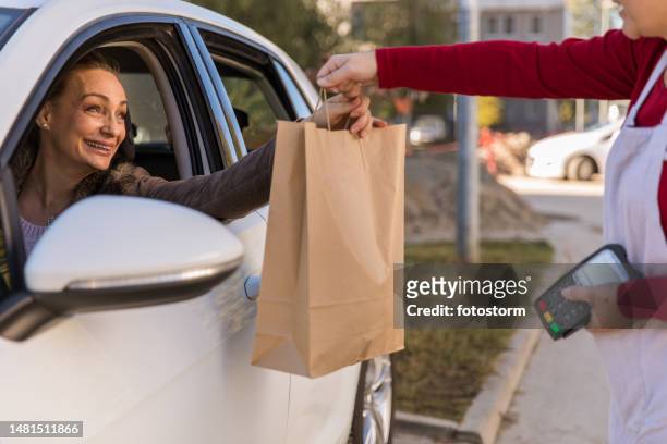 cheerful mature woman picking up her takeaway lunch in a drive through - curbside pickup 個照片及圖片檔
