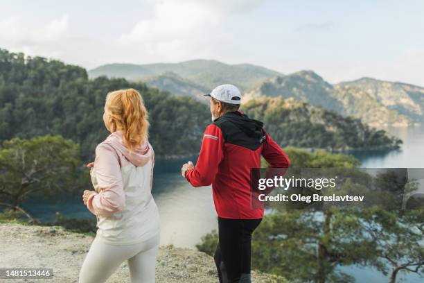 view from behind of senior couple running with scenery moiuntain and coastline view - vista posterior stock pictures, royalty-free photos & images