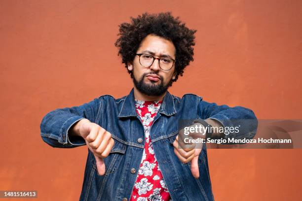 latino non-binary person with glasses and afro hairstyle giving a thumbs down - afwijzing stockfoto's en -beelden