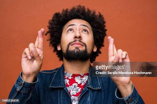 latino non-binary person with glasses and afro hairstyle crossing his fingers in hope, wishing - fingers crossed stock pictures, royalty-free photos & images
