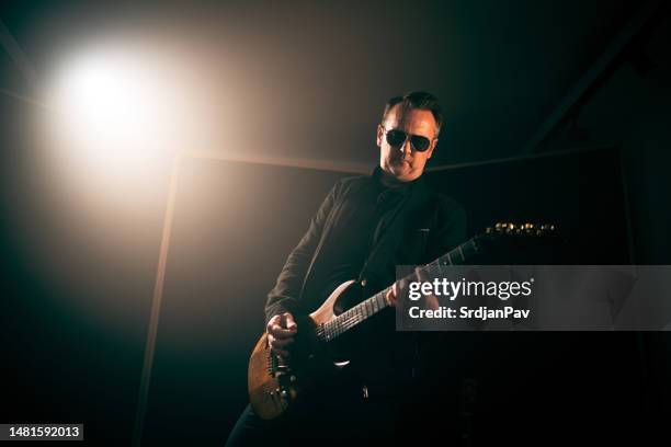 mid-adult male musician playing electric guitar at recording studio - bass guitar stock pictures, royalty-free photos & images