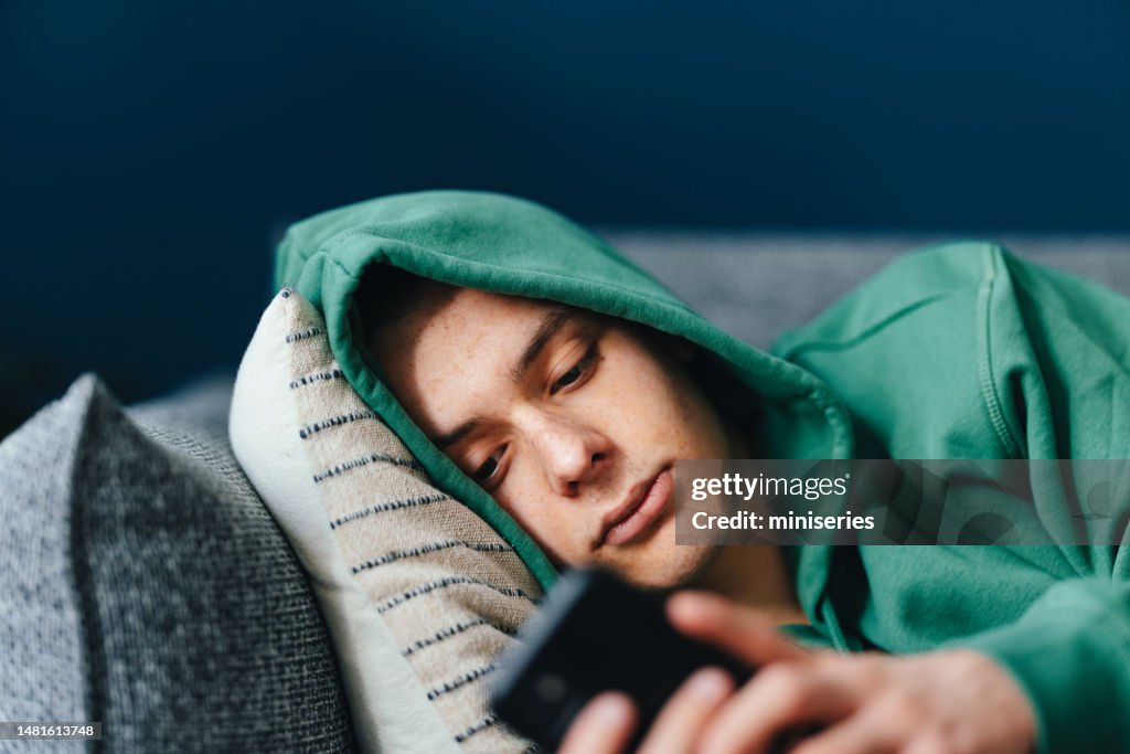 Sad Teenage Boy Using A Mobile Phone In His Bedroom