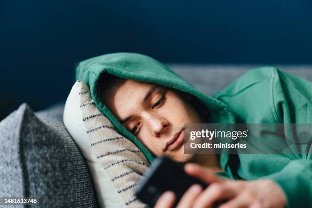 sad teenage boy using a mobile phone in his bedroom - depressed teenager stock pictures, royalty-free photos & images