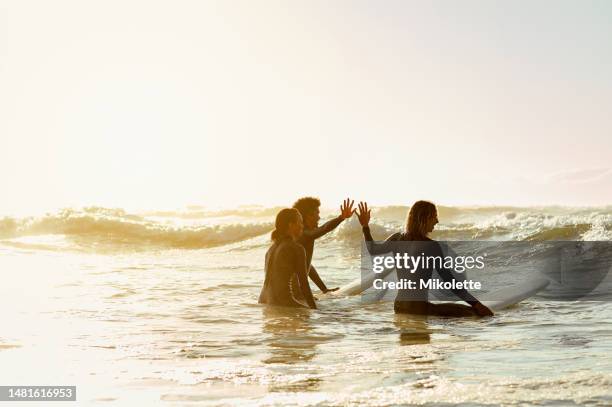 high five, surfer group and friends in sea ready for water sport in the ocean. beach mockup, vacation sunset and motivation of young people together with a surfboard about to start surfing - lakeshores stock pictures, royalty-free photos & images