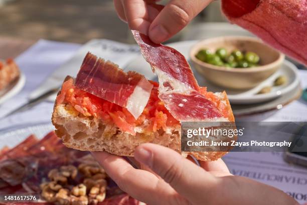 hand putting serrano ham on top of a slice of toasted bread with crushed tomato on top - tapas stock-fotos und bilder