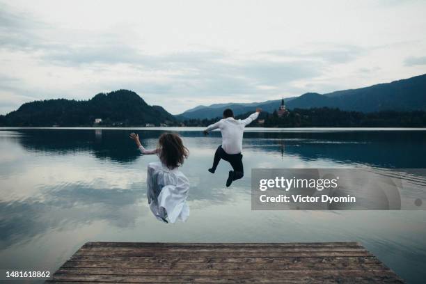 newlyweds jump into the cold mountain lake from the pier - wedding celebration stock pictures, royalty-free photos & images