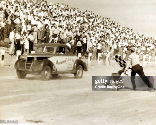Late-1940s: Ed Samples takes the checkered flag to win a Modified stock car race at Lakewood Speedway. Samples was driving a car owned by Wayne...