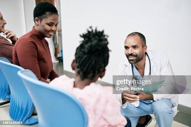 doctor talking with young family sitting in hospital waiting room - loungeroom stockfoto's en -beelden