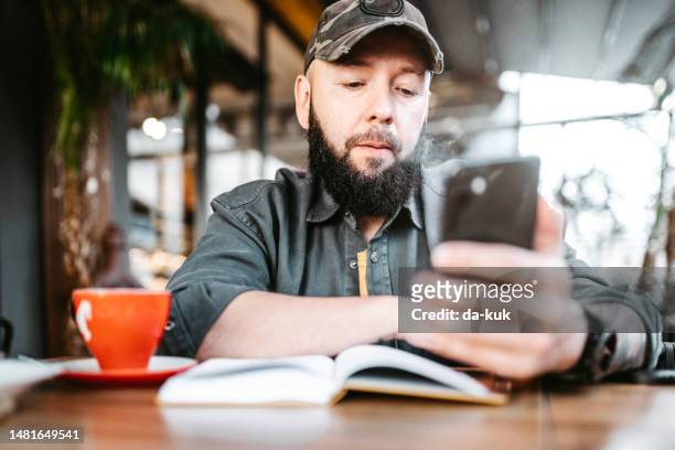 morning coffee before work. casual man using phone and note pad sitting in cafe - café da internet stock pictures, royalty-free photos & images
