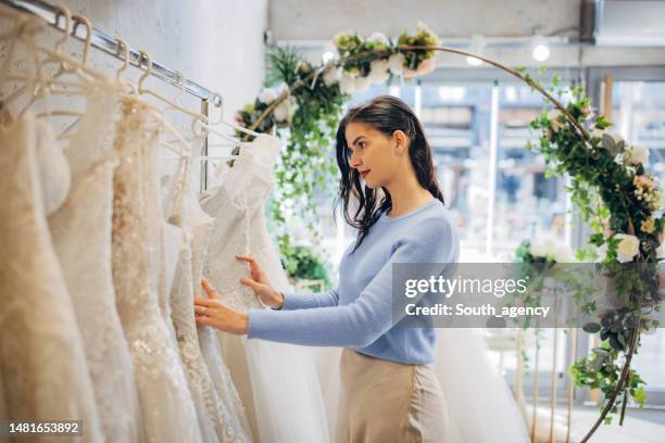 bride to be looking at the wedding dresses at the bridal shop - trouwjurk stockfoto's en -beelden