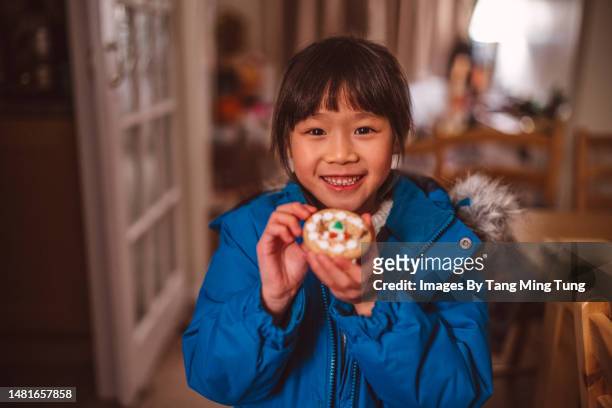 smiling lovely little girl holding a handmade cookie at home from her girl guiding's brownies activity - girl guide association stock pictures, royalty-free photos & images