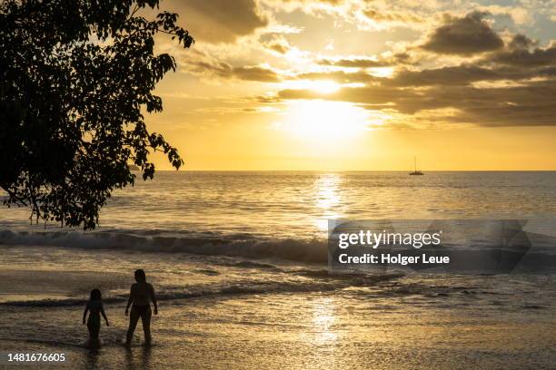 silhouette of mother and daughter at flamingo beach with catamaran in distance at sunset - guanacaste catamaran stock pictures, royalty-free photos & images