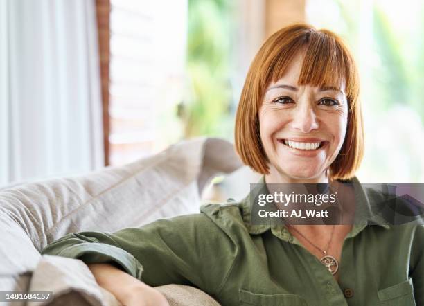 woman smiling while relaxing at home on her living room sofa - redhead stock pictures, royalty-free photos & images