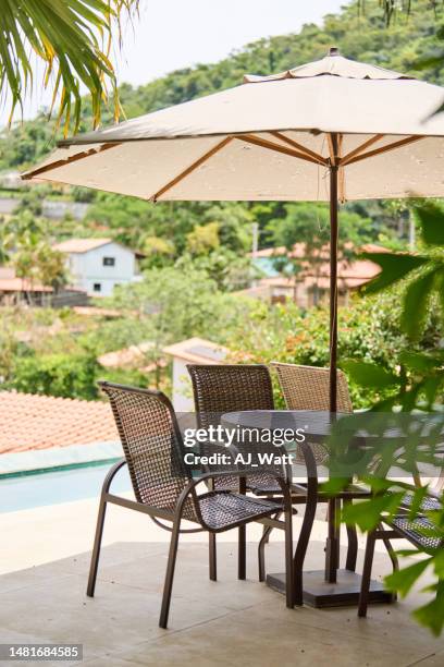 patio table and chairs with an umbrella sitting by a pool in summer - parasols stockfoto's en -beelden