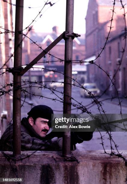 British army marksman provides cover for his patrol as it passes between concrete security bollards sited on the interface dividing Catholic and...