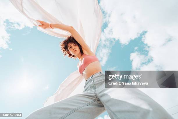 a beautiful asian woman with curly hair is dancing, waving a white cloth, wide angle shot from below - froschperspektive stock-fotos und bilder