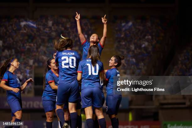 a latina female soccer player raises her arms in praise as she is lifted up into the air. - fußballliga stock-fotos und bilder