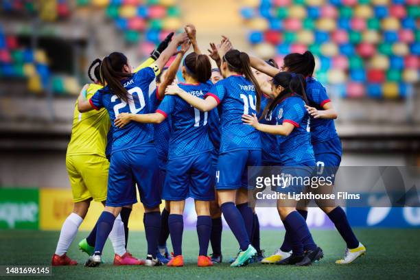 excited team of women football players raise their arms in a team huddle - competición por equipos fotografías e imágenes de stock