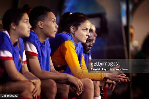 side view of professional soccer players on reserve as they watch their teammates play in a soccer match - reserve athlete - fotografias e filmes do acervo