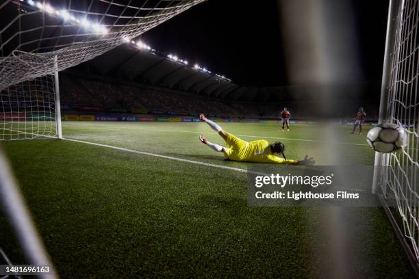 action rear view of a female soccer goalie diving and narrowly missing the ball before it goes in the goal - rete di calcio foto e immagini stock