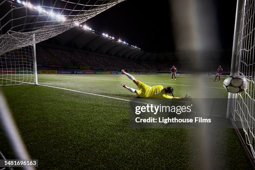 Action rear view of a female soccer goalie diving and narrowly missing the ball before it goes in the goal Action rear view of a female soccer goalie diving and narrowly missing the ball before it goes in the goal