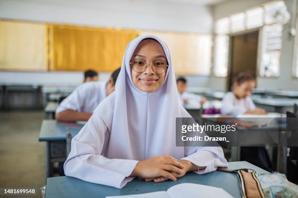 portrait of elementary schoolgirl in muslim school, wearing hijab, school uniform and looking at camera - hijab student stock pictures, royalty-free photos & images