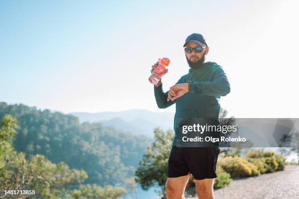 tired male trail runner with bottle of water checking heartbeat using smart watches while training in mountain area - turkey hunting 個照片及圖片檔