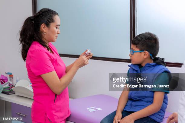 doctora pediatra preparando una jeringa para inyectar a un niño en su consultorio medico - pediatra stock-fotos und bilder