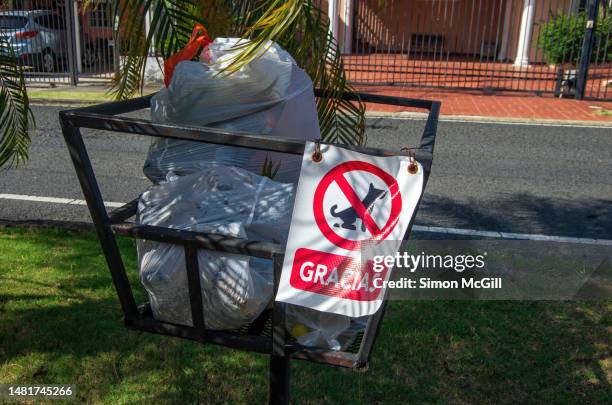 spanish-language sign statin g 'gracias' [thanks] forbidding dog feces in the raised pedestal metal waste basket for trash bags awaiting kerbside waste collection in a panama city residential neighborhood - dog waste bin stock pictures, royalty-free photos & images