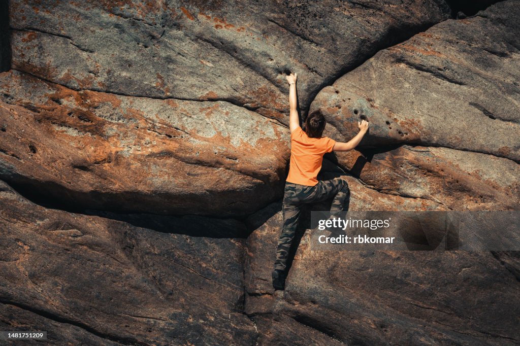 Agile brave woman climbing a rocky wall - climber striving for the top
