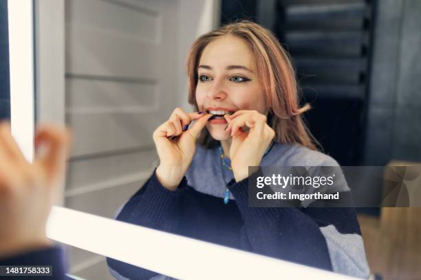 teenage girl is putting on her transparent dental aligner in the bathroom - dental aligners stock pictures, royalty-free photos & images