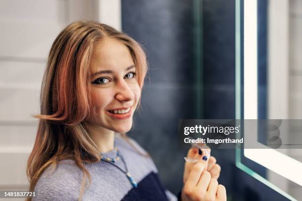 teenage girl is putting on her transparent dental aligner in the bathroom - invisalign stockfoto's en -beelden