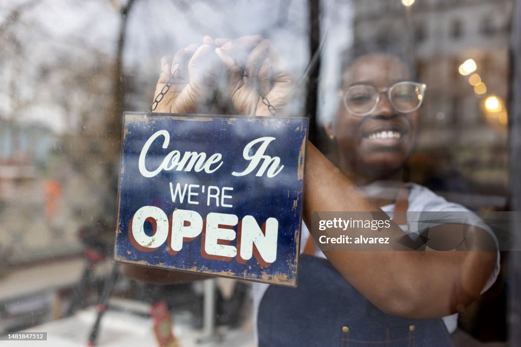 Afrikanerin hängt ein offenes Schild an die Glastür eines Zero-Waste-Lebensmittelgeschäfts