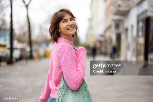 attractive young woman looking behind while walking outdoors on city street - pink color stock pictures, royalty-free photos & images
