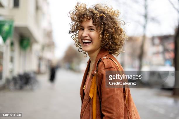 beautiful woman walking outdoors looking behind and laughing - city life stock pictures, royalty-free photos & images