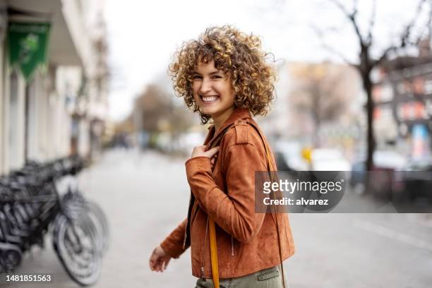 mujer sonriente caminando al aire libre en la calle de la ciudad mirando hacia atrás - mujeres de mediana edad fotografías e imágenes de stock