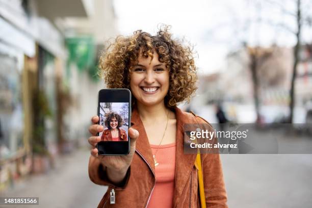 femme mi-adulte joyeuse montrant sa photo sur son téléphone portable - demonstration photos et images de collection