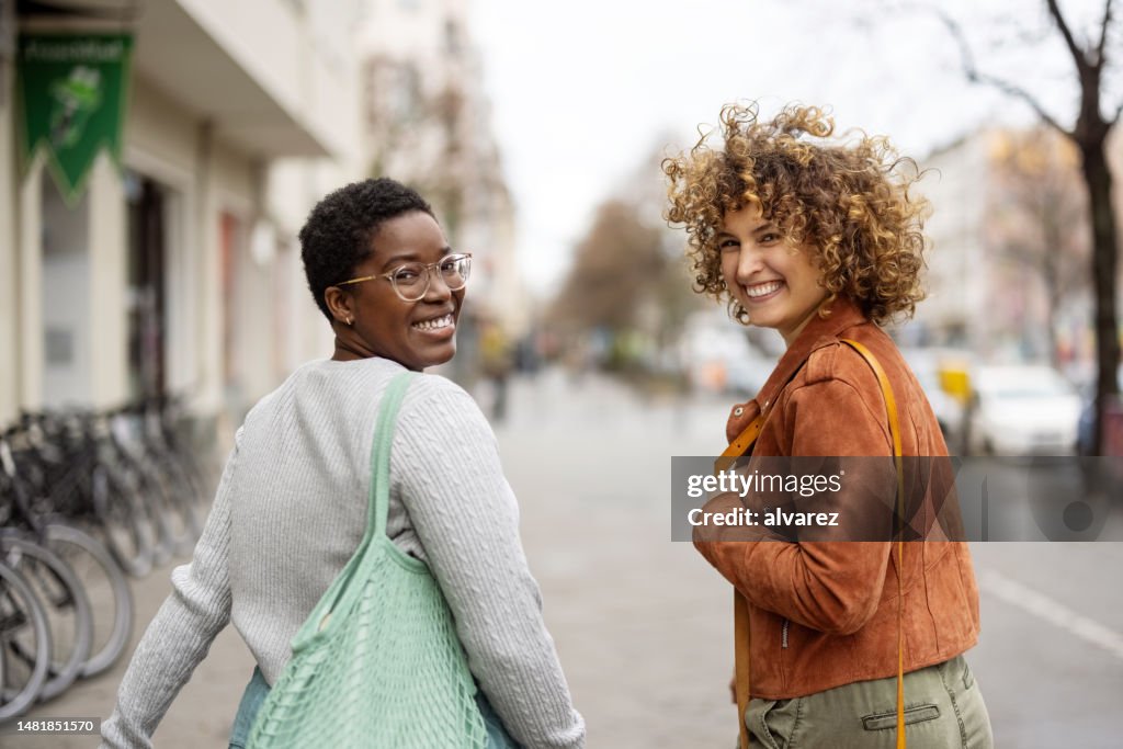 Two women friends walking down the street and looking behind
