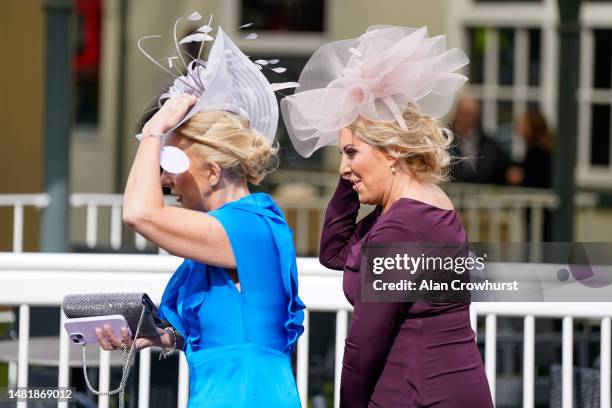 Racegoers hold onto their hats as strong winds arrive at Aintree Racecourse on April 13, 2023 in Liverpool, England.