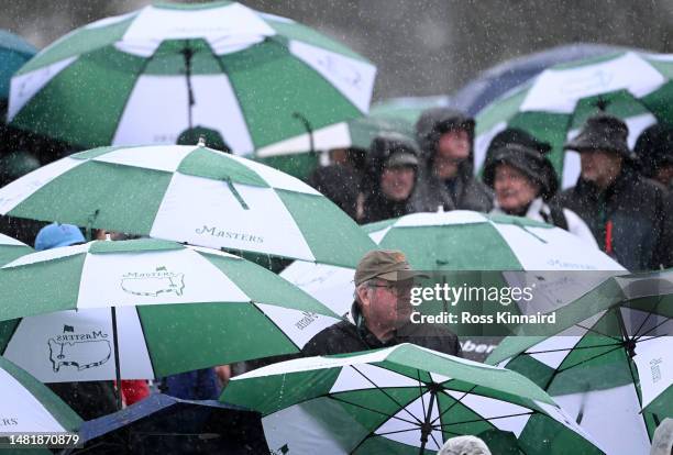 Patrons take cover from the rain around the 18th green during the third round of the 2023 Masters Tournament at Augusta National Golf Club on April...