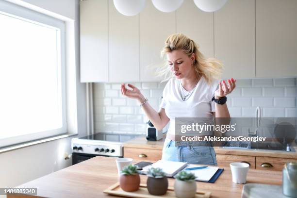 schöne blonde frau, die sich verwirrt fühlt, während sie freiberuflich arbeitet und gleichzeitig in der küche kocht - lady cooking confused stock-fotos und bilder