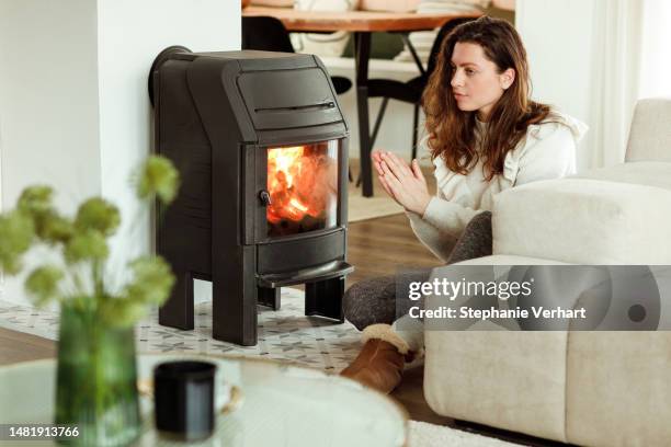 woman trying to keep warm by warming hands near the fireplace in winter time - log fire stock pictures, royalty-free photos & images