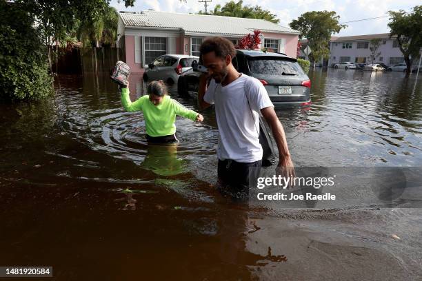 Katherine Arroyo and James Richard walk through a flooded street after record rains fell in the area on April 13, 2023 in Hollywood, Florida. The...