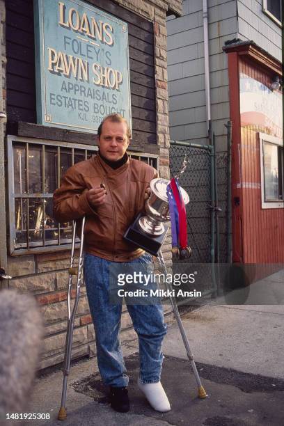 Portrait of American actor Michael Chiklis as he poses, on a pair of crutches, with a cigar in one hand and a trophy in the other, during the filming...