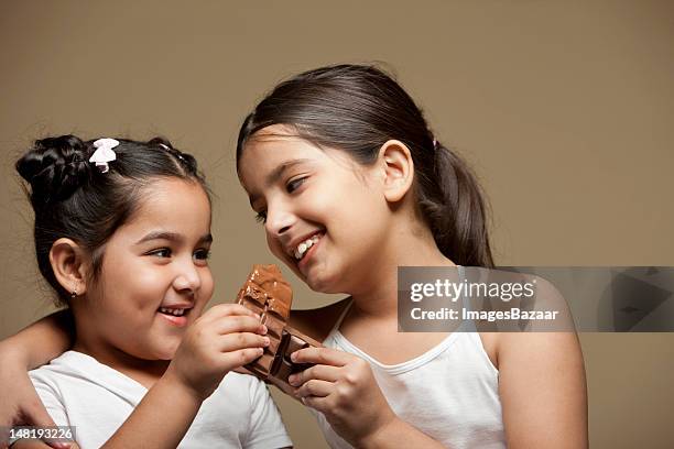 studio portrait of two sisters (6-11) eating chocolate - sharing chocolate stock pictures, royalty-free photos & images