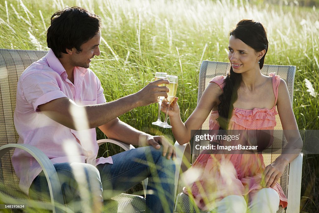 Young couple drinking champagne surrounded by tall grass