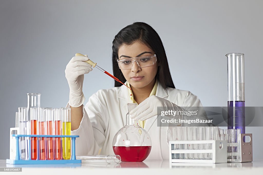 Young woman in laboratory dripping liquid into glassware