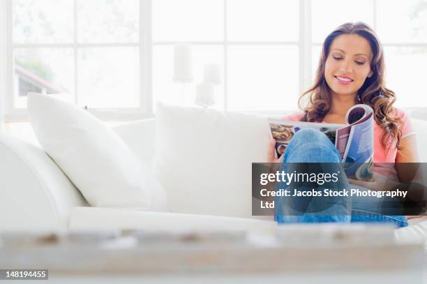 hispanic woman sitting on sofa reading magazine - magazine stock pictures, royalty-free photos & images